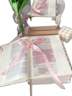 an open book with pink ribbon and tulips sitting on top of it next to a vase filled with flowers