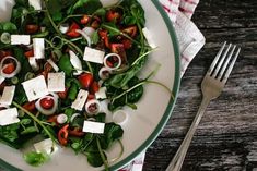 a white plate topped with salad next to a fork and knife on top of a wooden table