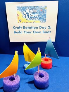 three small toy boats sitting next to each other on a blue tablecloth with a sign in the background