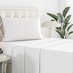 a bed with white sheets and pillows next to a plant