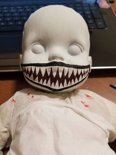 a creepy doll is sitting in front of a laptop computer, with its mouth open