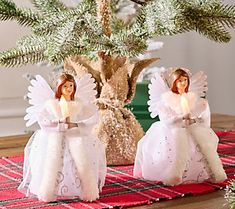 two angel figurines sitting on top of a table next to a christmas tree