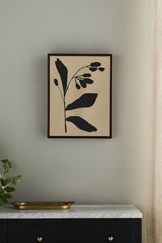 a black and white painting hanging on the wall next to a table with a plant in it