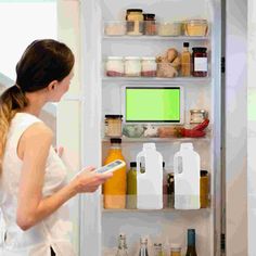 a woman standing in front of an open refrigerator holding a tablet and looking at it