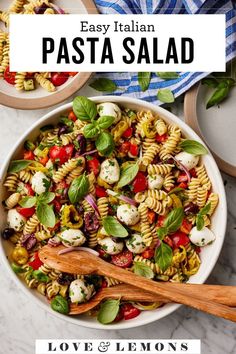 pasta salad in a white bowl with basil leaves and tomatoes on top, next to a wooden spoon