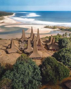 an aerial view of some huts on the beach with water and trees in the foreground