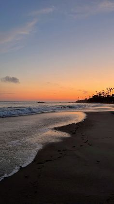 the sun is setting at the beach with footprints in the sand