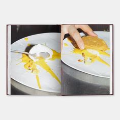 an open book with food on it and a spoon in front of the pages that have yellow paint splattered all over them