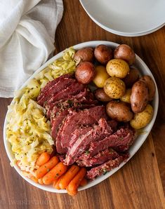 corned beef, potatoes and carrots on a white plate next to a fork