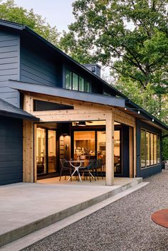 a modern house with an outdoor patio and dining area in the back yard, surrounded by trees