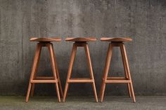 three wooden stools sitting next to each other on the cement floor in front of a concrete wall