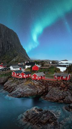 the aurora bore is visible above red houses on rocks in front of a body of water