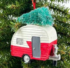 a red and white camper ornament hanging from a christmas tree with green needles