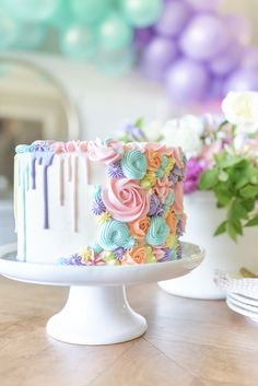 a colorful cake sitting on top of a wooden table next to flowers and balloons in the background