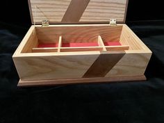 an open wooden box on a black surface with red paper in the bottom and inside