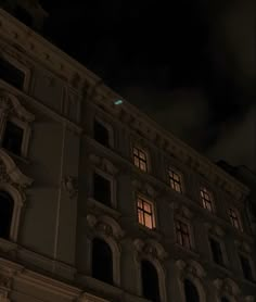 an old building lit up at night with the moon in the sky and clouds above it