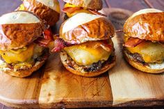 four burgers with bacon and cheese on a cutting board, ready to be eaten