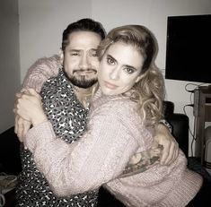 a man and woman hugging each other in a living room with a tv on the wall behind them