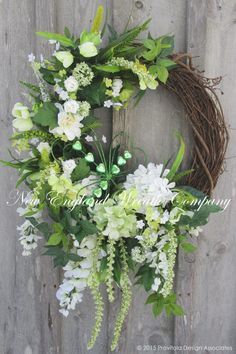 a wreath with white flowers and greenery hanging on a fence