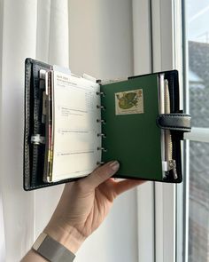 a person holding an open planner in front of a window