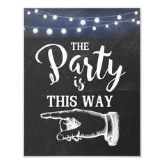 the party is this way sign with string lights on it and a hand pointing at something