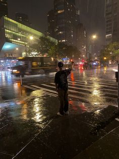 a man standing on the side of a street holding an umbrella in the rain at night