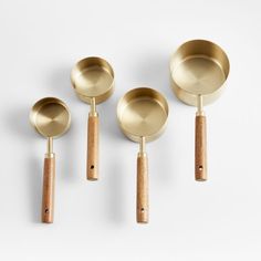 three brass measuring spoons with wooden handles and one without, on a white background