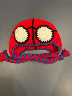 a crocheted red and blue hat with big eyes on the top, sitting on a gray surface