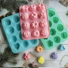 two trays filled with pink and blue icing next to pine cones on a white table