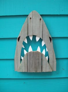 a wooden shark mask hanging on the side of a blue building with it's mouth open