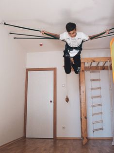 a young man is hanging upside down from the ceiling in an empty room with ladders