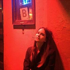 a woman sitting in front of a red wall with a neon sign above her head