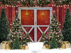 two christmas trees in front of a red barn with presents under the doors and snow on the ground