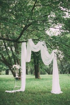 an outdoor wedding ceremony setup with white drapes and flowers on the grass under a tree