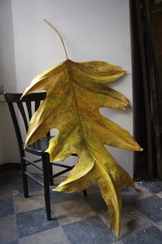 a large yellow leaf sitting on top of a black chair next to a white wall