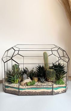 a glass terrarium with succulents and rocks in the bottom, on a white surface