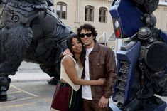 a man and woman standing in front of a giant godzilla statue with their arms around each other