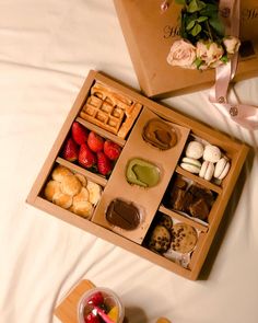 an open wooden box filled with different types of food on a white bed next to flowers