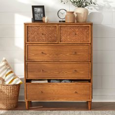 a wooden dresser with wicker drawers next to a plant