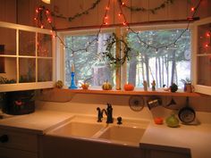 a kitchen sink under a window with christmas lights hanging from the windowsill above it