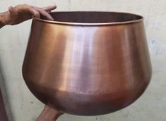 a person holding a large metal pot in their hand and touching it with the other hand