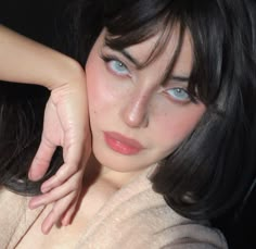 a woman with dark hair and blue eyes poses for the camera while holding her hand on her shoulder