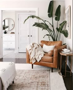 a living room with a brown leather chair and large plant in the corner next to it