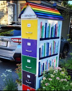 a multicolored bookcase is on the sidewalk next to some flowers and cars