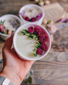 a person holding three bowls with flowers in them on a wooden table next to other bowls