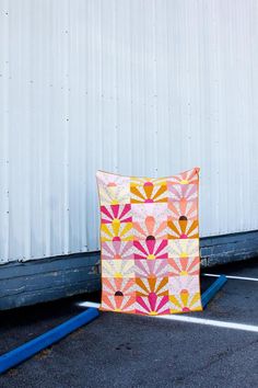 an orange and pink quilt sitting on top of a parking lot next to a building