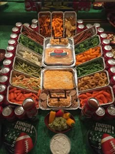 several trays of food are arranged on a football themed buffet table with drinks and snacks