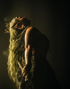 a woman with green hair and makeup holding a stick in her hand while standing on stage