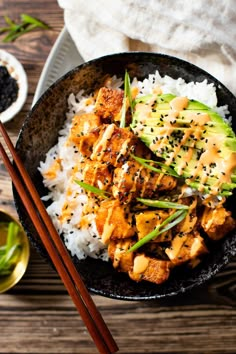 a black bowl filled with rice and chicken next to chopsticks on a wooden table