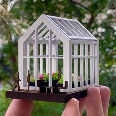 someone is holding up a miniature house made out of wood and plastic material with plants in it